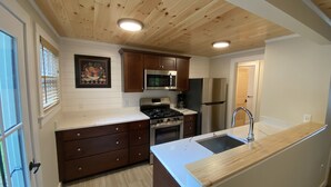A kitchen with wooden cabinets, a stainless steel refrigerator, a microwave, a stove, and a sink. - The Pines at Center Harbor (Moultonborough)