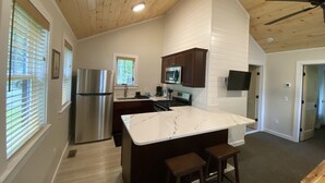 A modern kitchen with wooden ceiling, stainless steel appliances, a marble island, and bar stools. - The Pines at Center Harbor (Moultonborough)