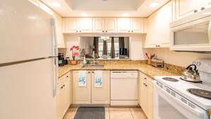 Une cuisine avec des meubles blancs, un plan de travail en granit, un four à micro-ondes, une cuisinière et une horloge murale.