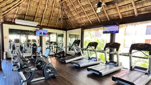 A gym with treadmills, elliptical machines, and weight equipment under a thatched roof. - Fully renovated top floor oceanfront condo. (Bucerias)