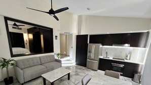 A modern living room with a sofa, coffee table, and a dining area with a marble table. There is a kitchen with a refrigerator and oven. - Fully renovated top floor oceanfront condo. (Bucerias)