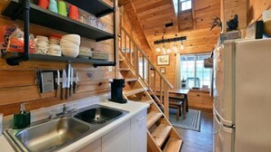 A wooden interior with a kitchen area, including a sink, shelves with kitchenware, and a staircase leading to another room. - Cozy Hayward Moose Lake Getaway (Hayward)