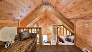 A cozy attic bedroom with wooden walls and a sloped ceiling, featuring a bed with a blanket and pillows, and a second bed with a plaid blanket. - Cozy Hayward Moose Lake Getaway (Hayward)