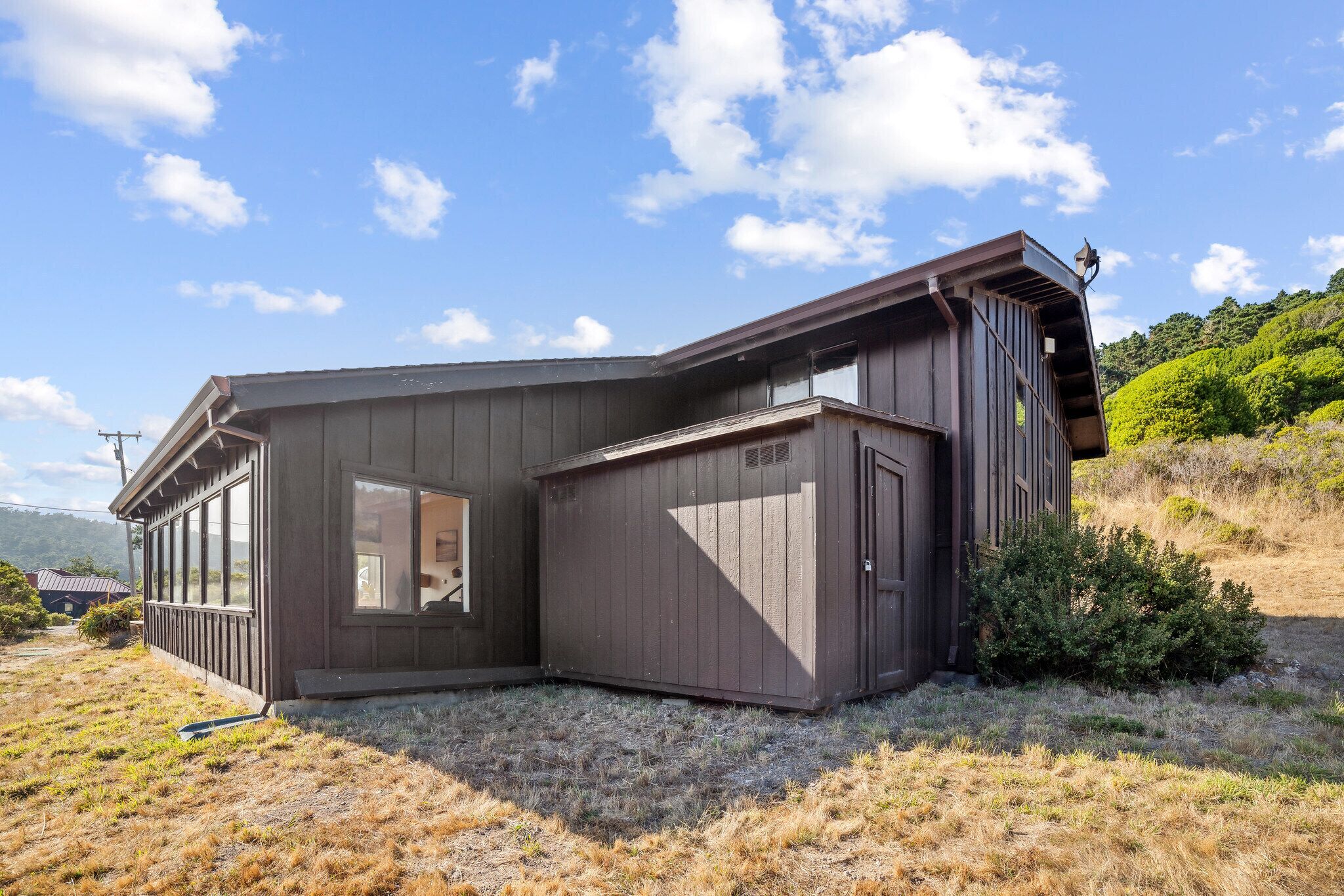 Ett modernt hus med ett stort garage, en inglasad veranda och utsikt över en grönskande sluttning.