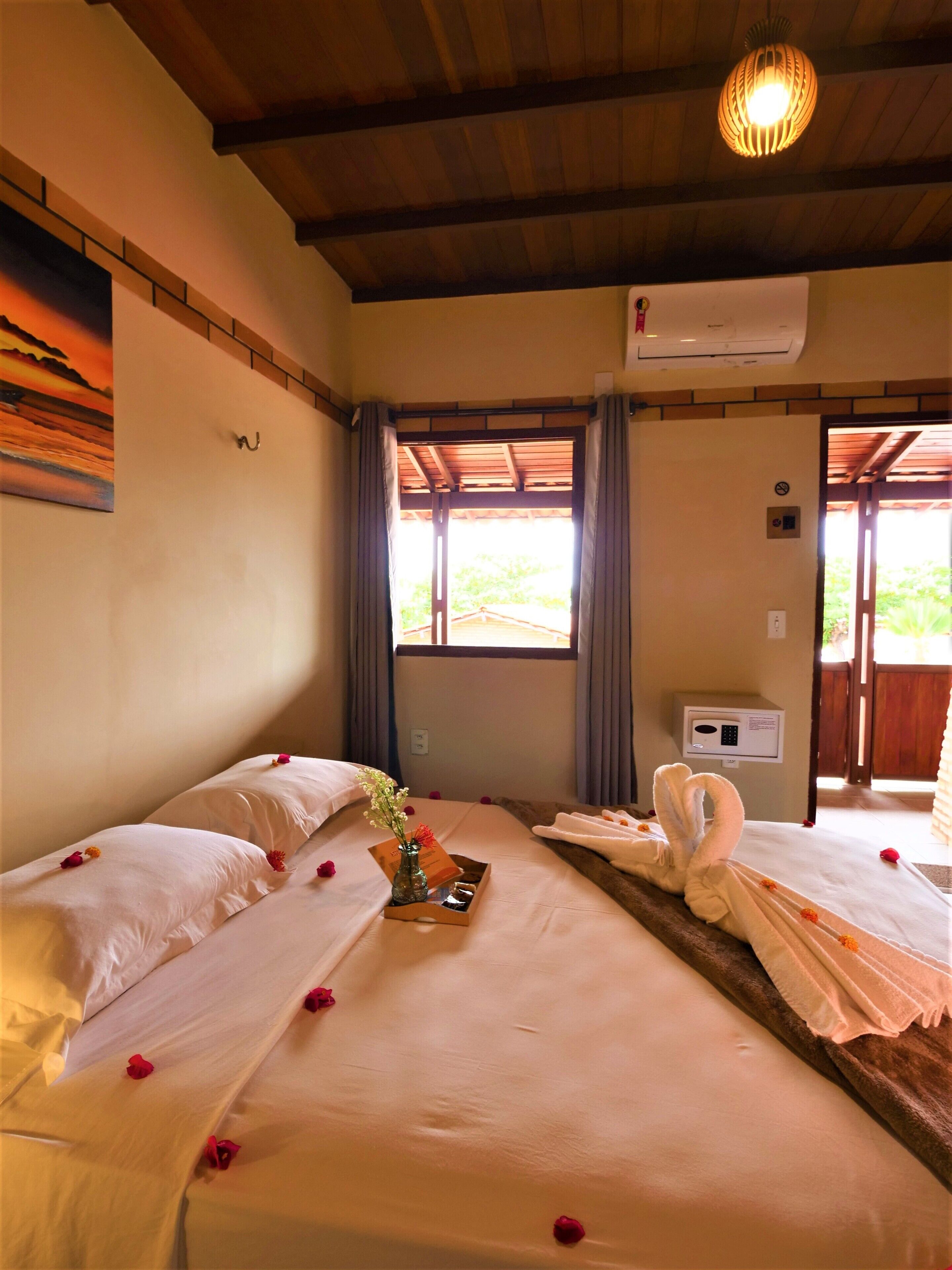 Habitación de hotel con dos camas, techo de madera, unidad de aire acondicionado, ventana con cortinas y panel de control en la pared.