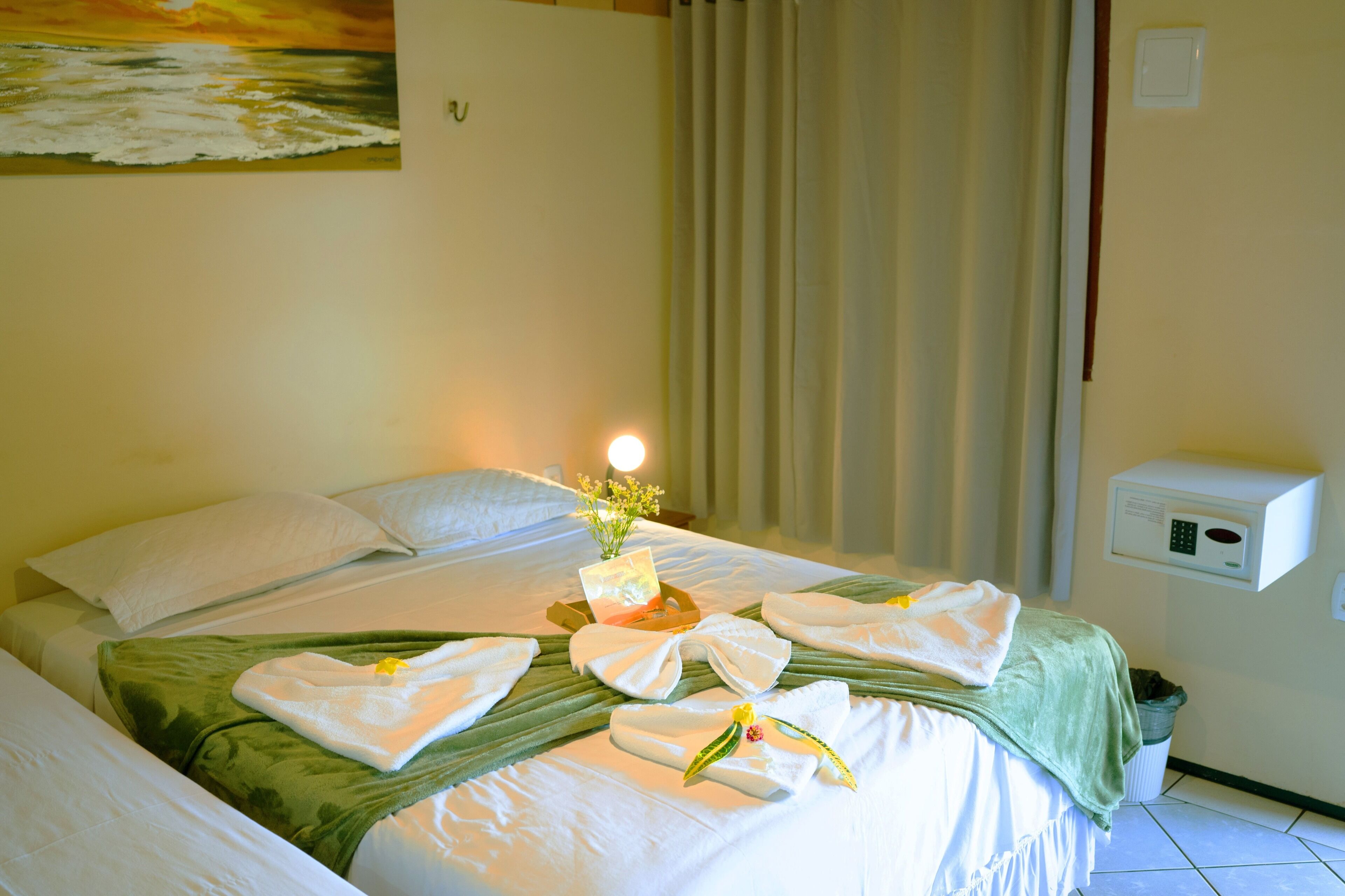 A hotel room with a neatly made bed, a bedside table with a lamp, a painting on the wall, and a window with curtains.