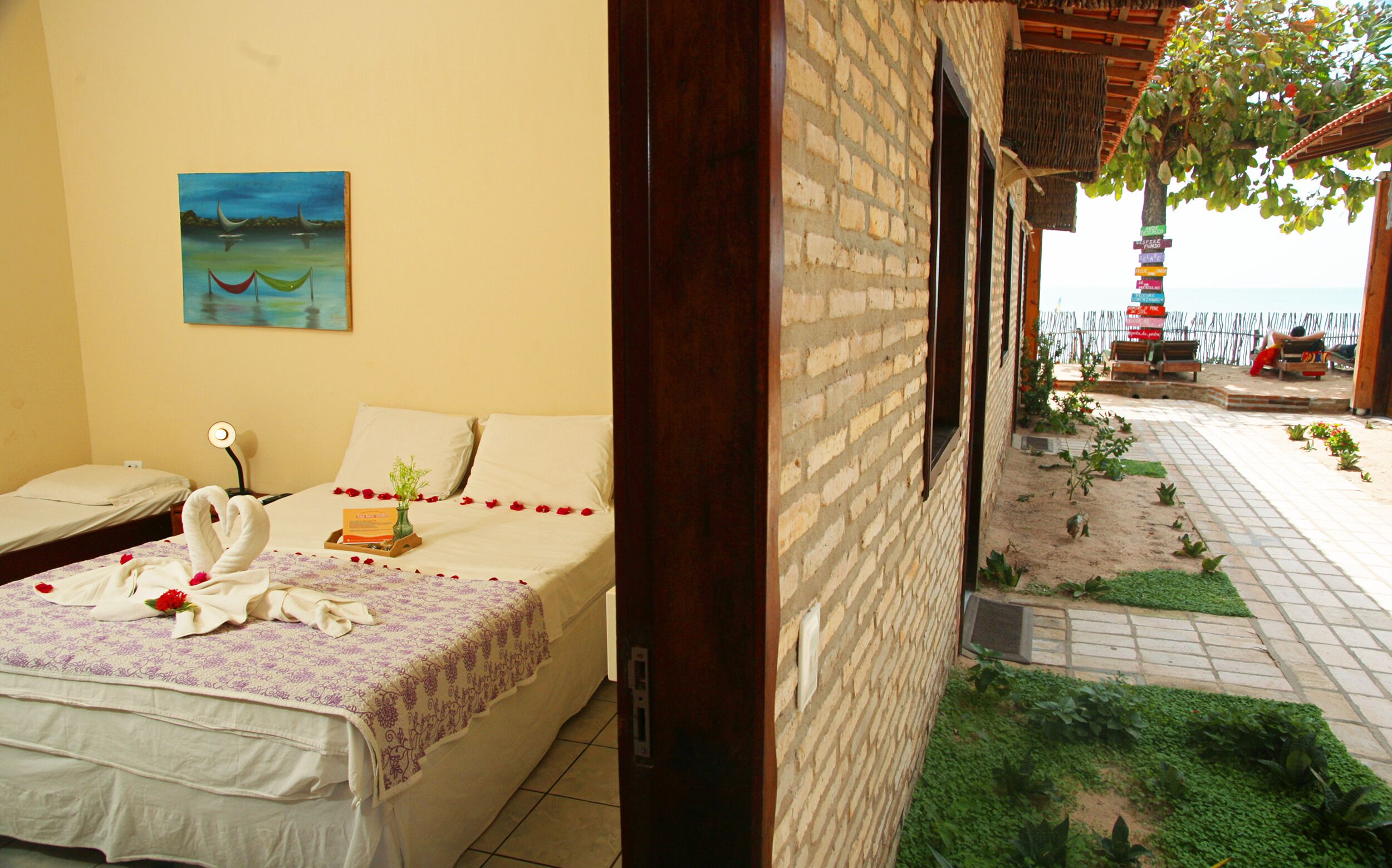A hotel room with a bed, a painting, and a view of the beach and a tower.
