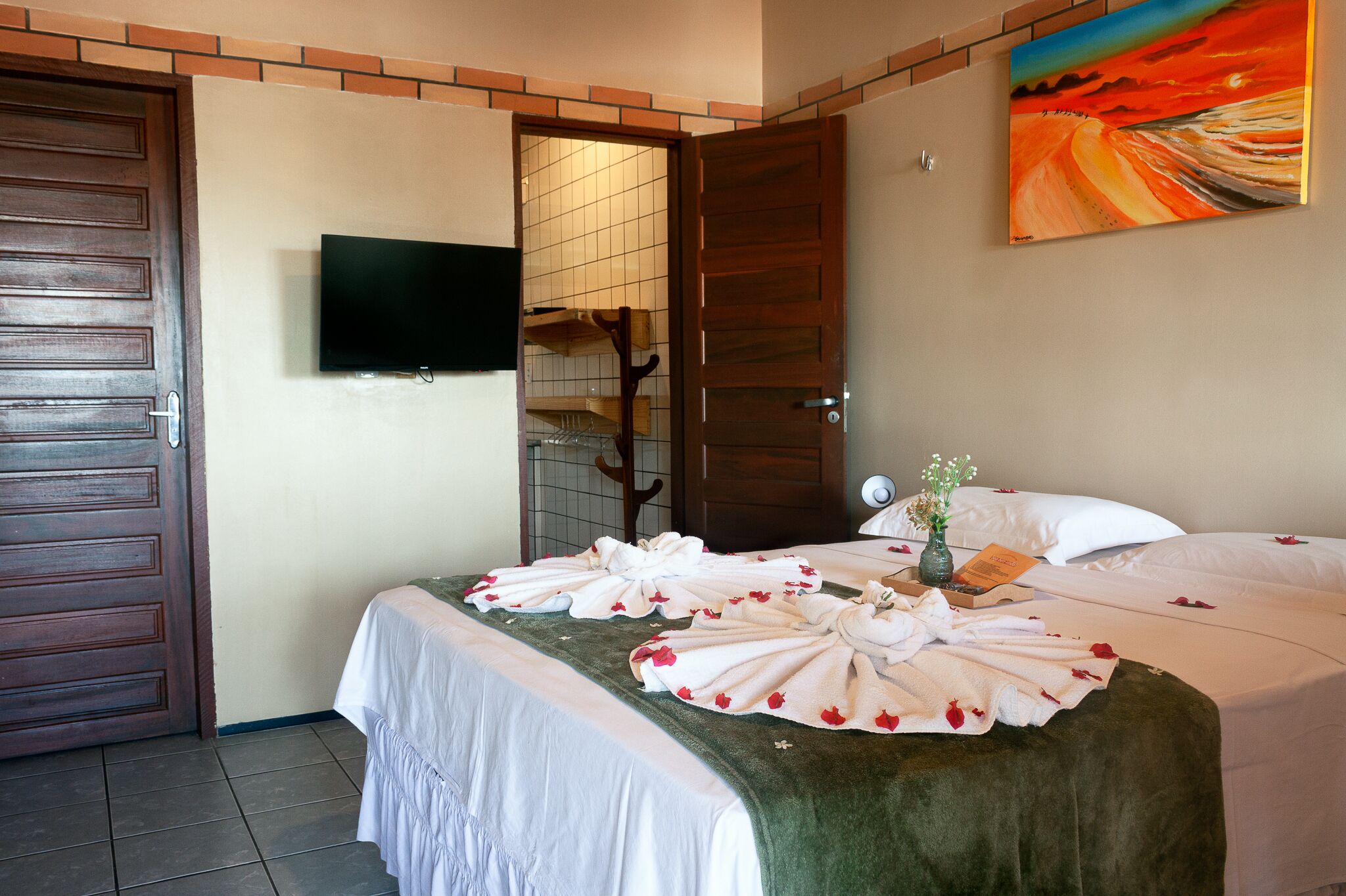 A hotel room with a bed, a TV mounted on the wall, and a painting above the bed.