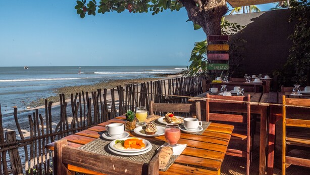 Ein Holztisch mit Essen und Getränken, mit Blick auf einen Strand, Wellen und ein entferntes Boot.