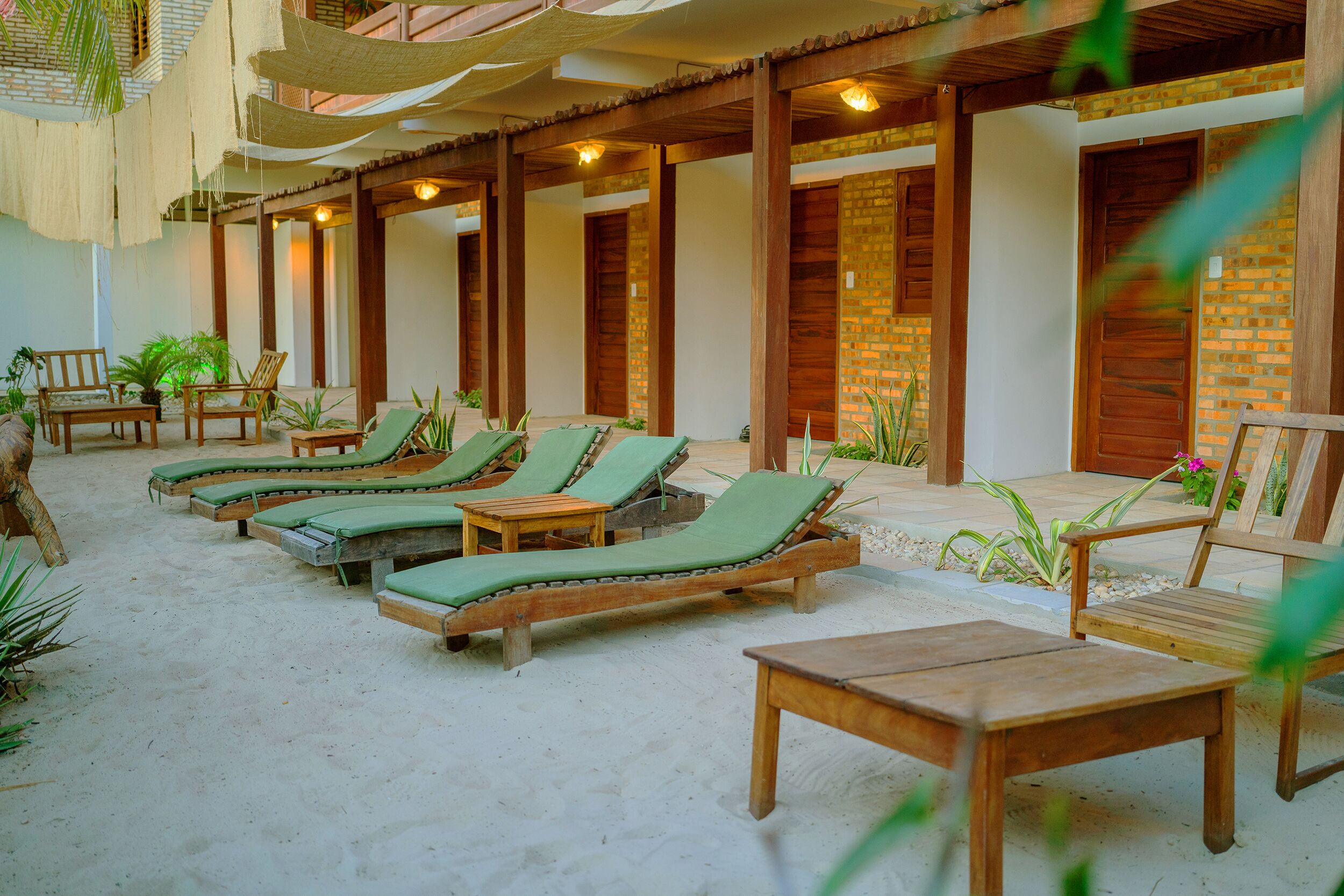 A sunlit outdoor lounge area with wooden loungers and tables, surrounded by brick walls and potted plants.