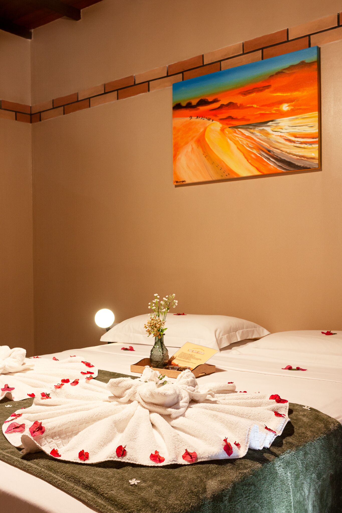 Ein Hotelzimmer mit Bett, Blumen in einer Vase und einem Gemälde an der Wand.