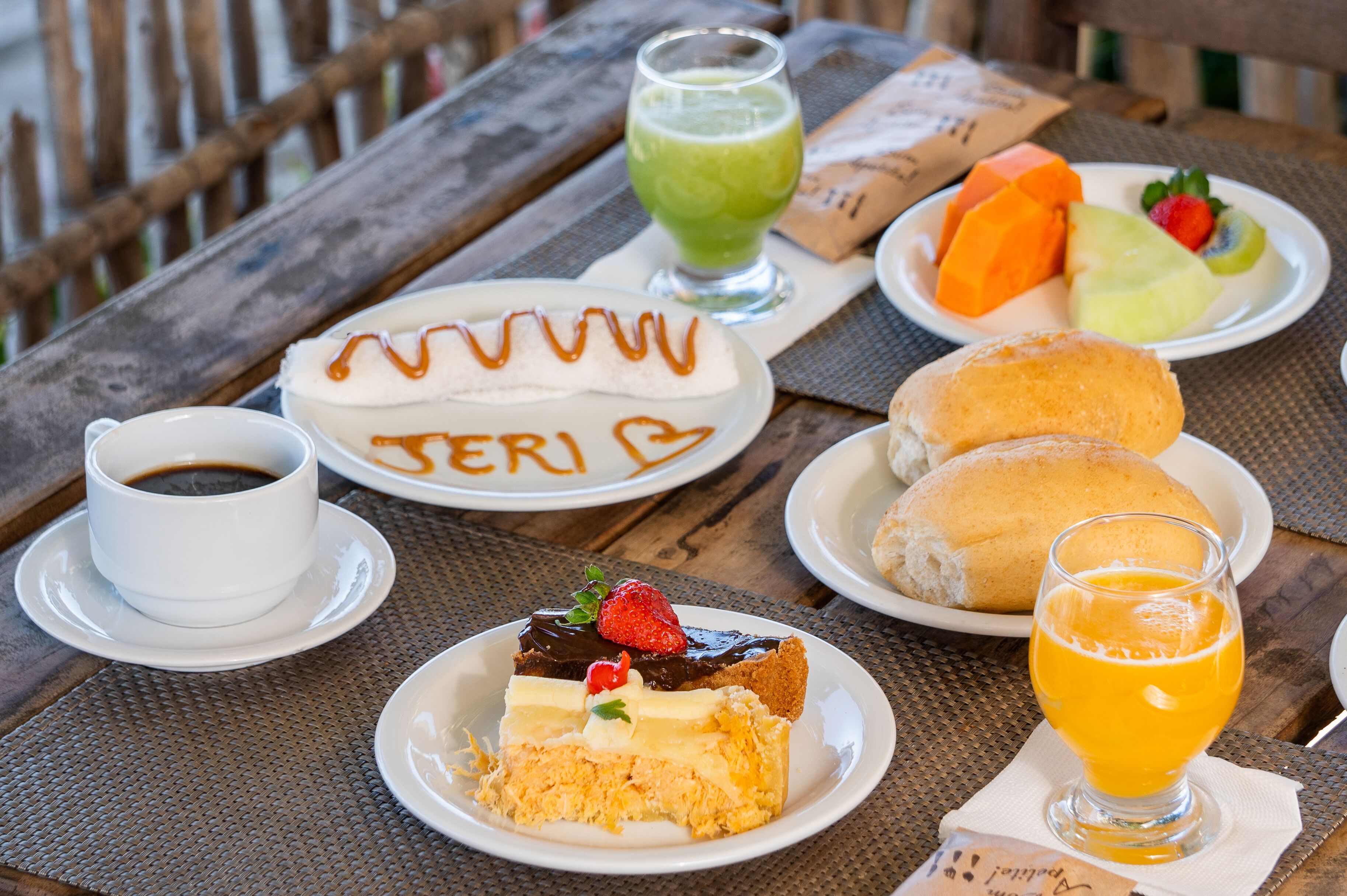 Una mesa con diferentes alimentos, incluyendo un pastel con la palabra 'TERI', un vaso de jugo verde, un plato de fruta y un vaso de jugo de naranja.