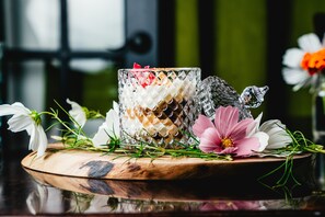 A decorative glass container with a wooden base, surrounded by flowers and greenery. - Twisted Lemon Restaurant & Boutique Inn (Haldimand County)