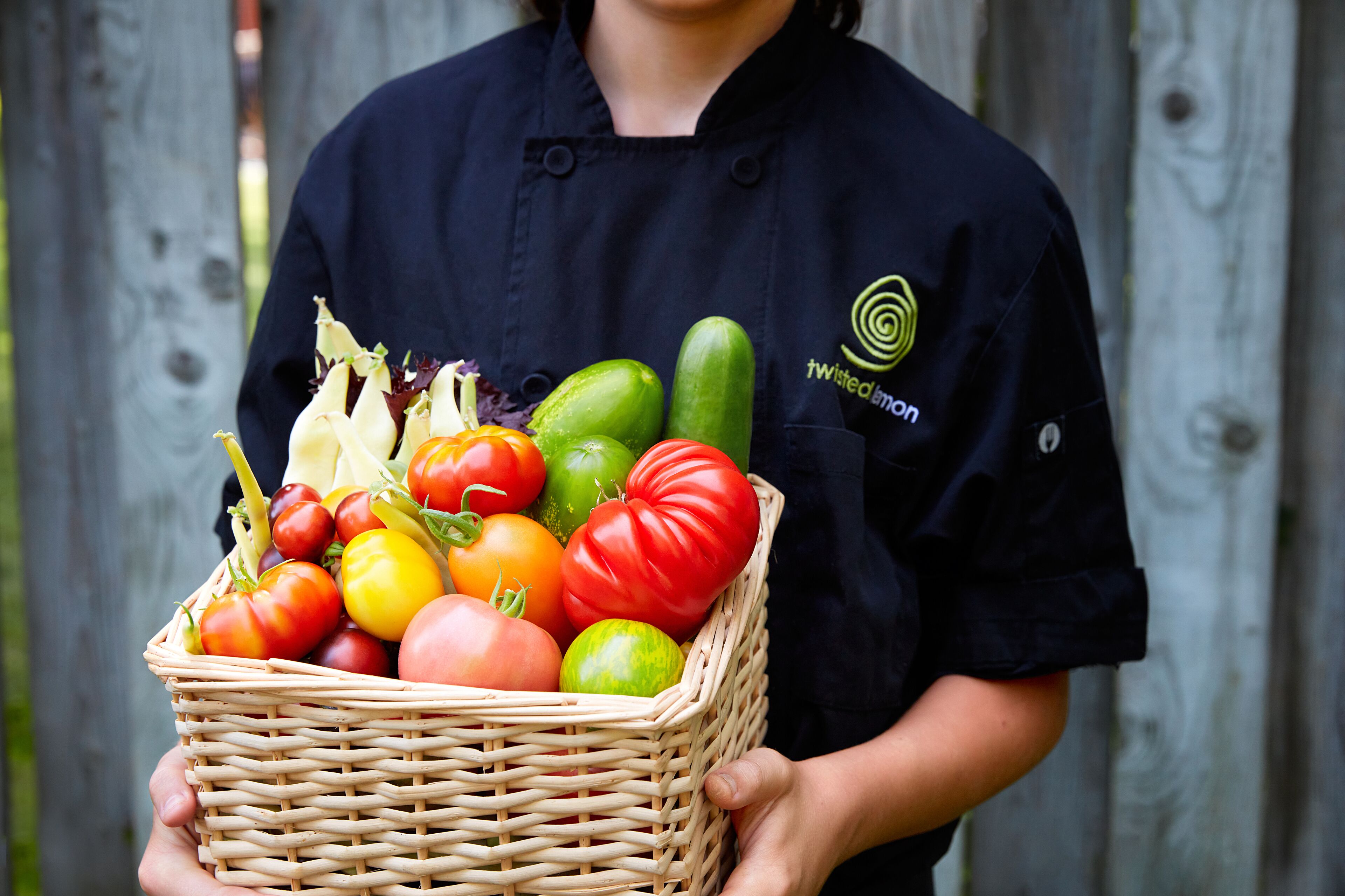 Una persona sostiene una cesta de mimbre llena de diversos vegetales.