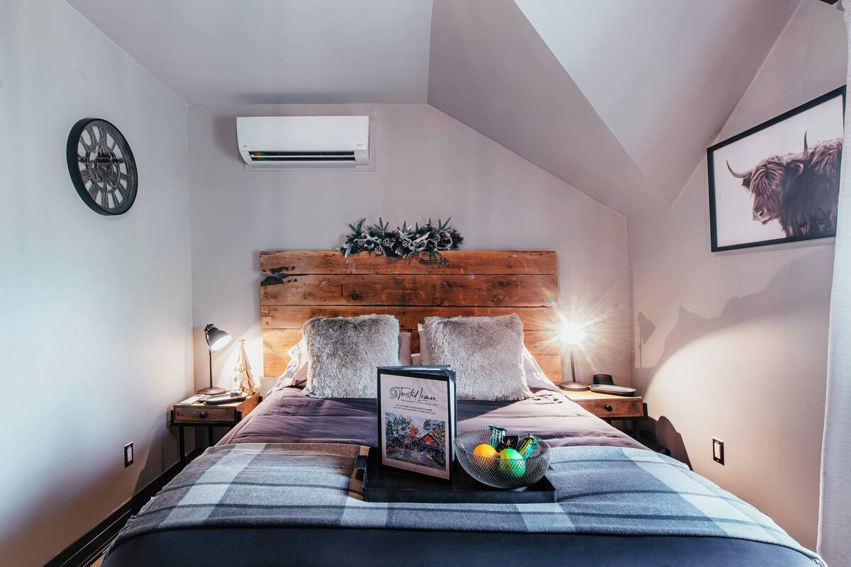 Une chambre à coucher avec une tête de lit en bois, une table de chevet avec une lampe, un tableau encadré et un panier rempli d’oranges.