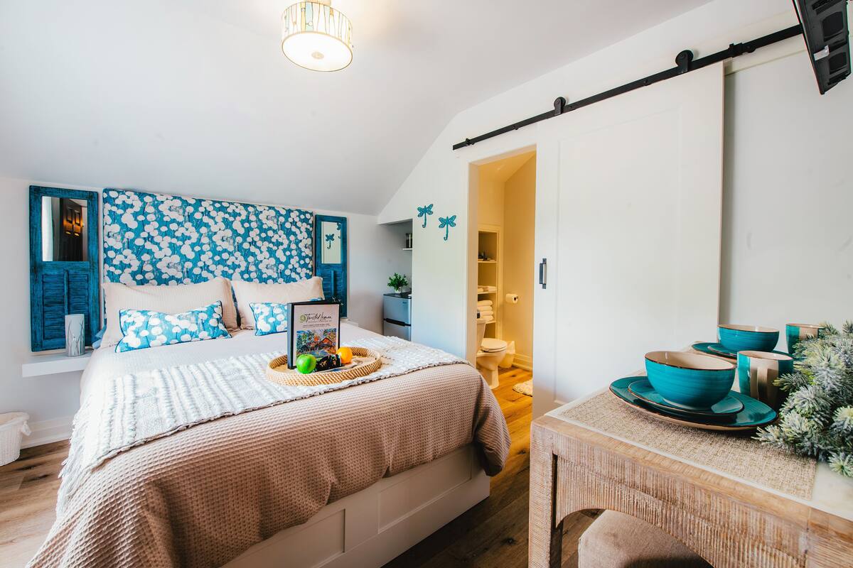 Une chambre à coucher avec un lit, une table de chevet sur laquelle se trouve un bol, et un mur orné d’un motif bleu et blanc.