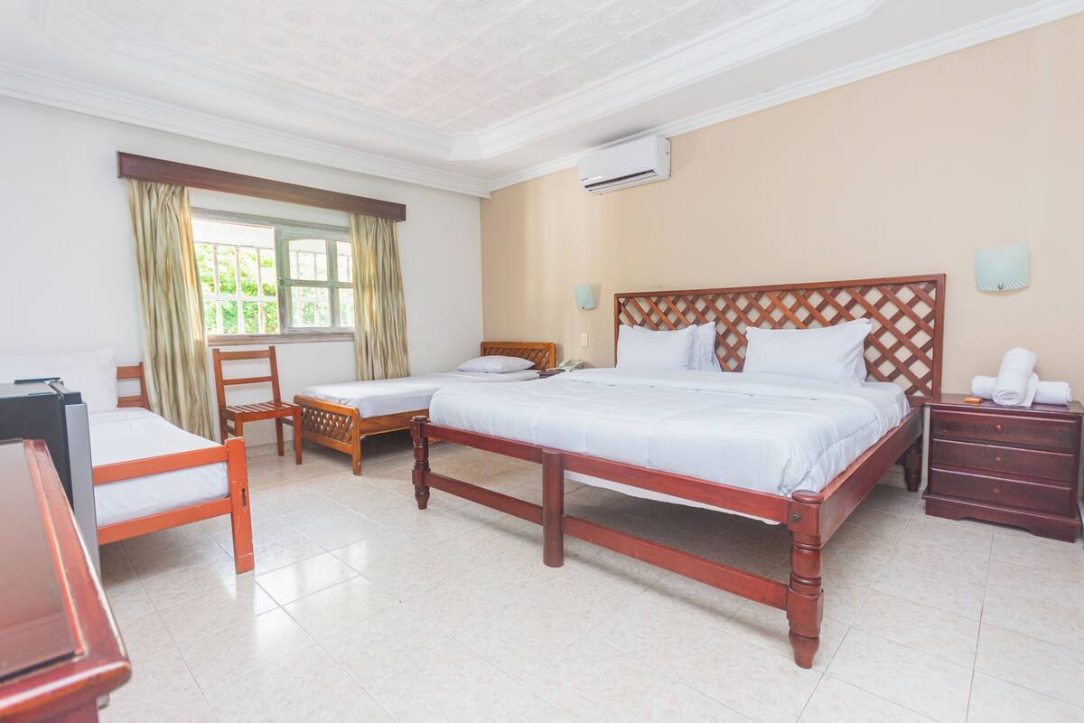 A hotel room with a large bed, a smaller bed, a desk, a chair, a nightstand, and a window with curtains.