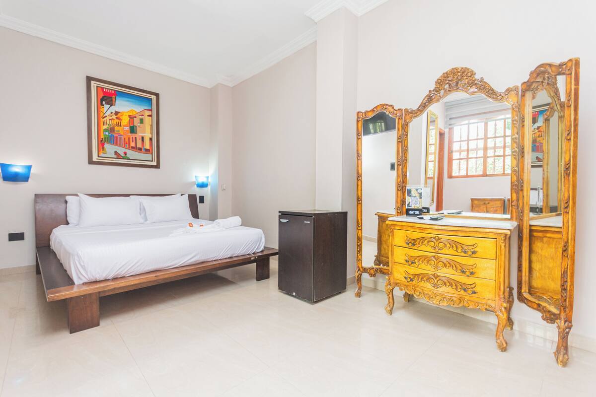 A hotel room with a bed, a dresser, a mirror, and a small refrigerator.