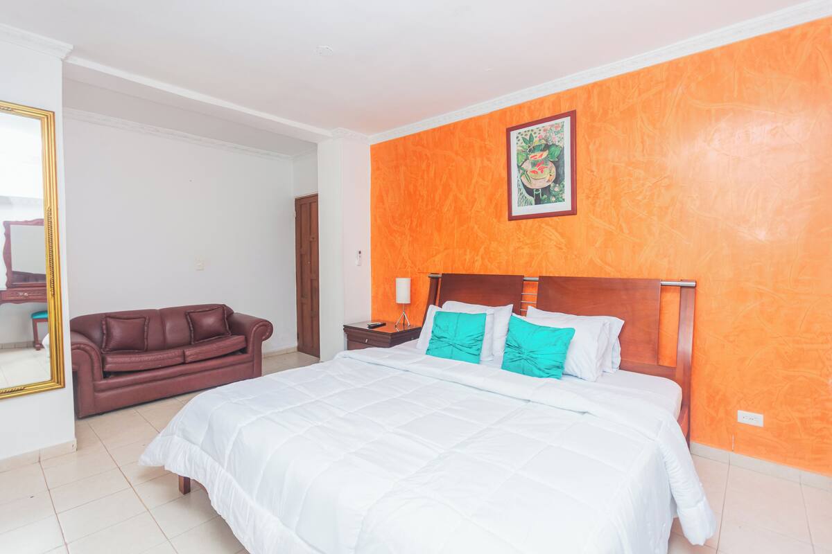 A bedroom with a large bed, a brown leather sofa, and an orange accent wall.