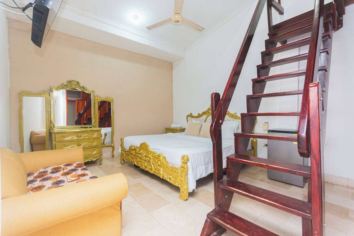 A bedroom with a bed, a dresser, a mirror, and a wooden staircase.