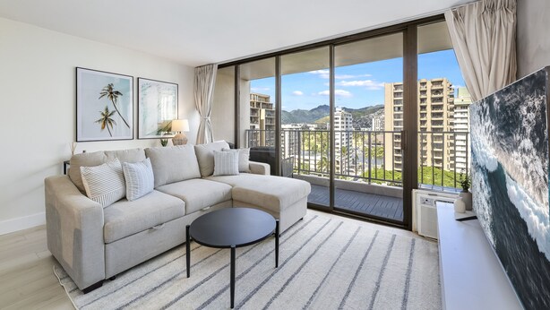 A modern living room with a beige sectional sofa, a round coffee table, and a large window offering a city view.