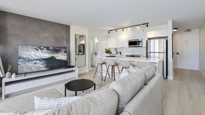 A modern living room with a large flat-screen TV, a grey sofa, and a small round table.