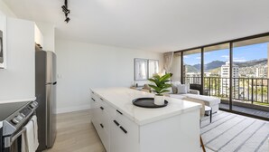 A modern kitchen with a large island, a built-in oven, and a view of the city through large windows.