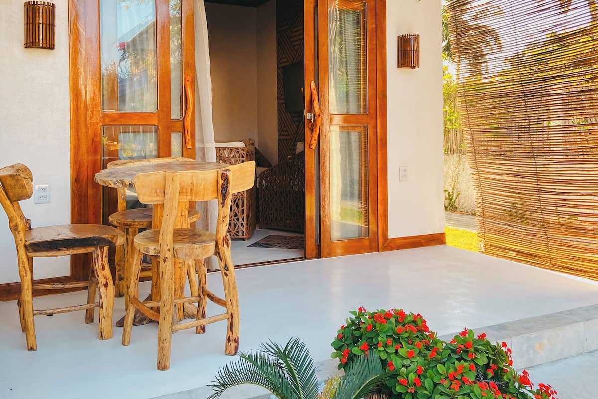 Une porte en bois avec des panneaux de verre, une table en bois avec des chaises, et un petit jardin avec des fleurs rouges.