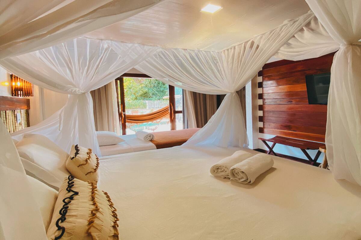 Une chambre avec un lit sous un dais, un banc et une vue sur l’extérieur.