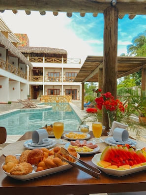 A breakfast table with a pool view, including bread, fruit, and juice. - Pousada Velho Chico (Amontada)