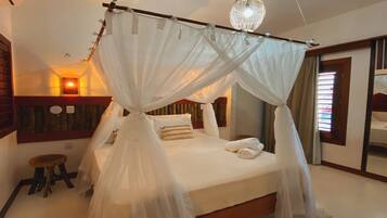 A bedroom with a four-poster bed, a small stool, and a wall-mounted light fixture.