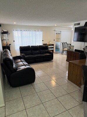 A living room with a black leather sofa, a wooden coffee table, and a television mounted on the wall. - Make The Palm Home your home and the best pleasant stay with awesome amenities (Glendale)