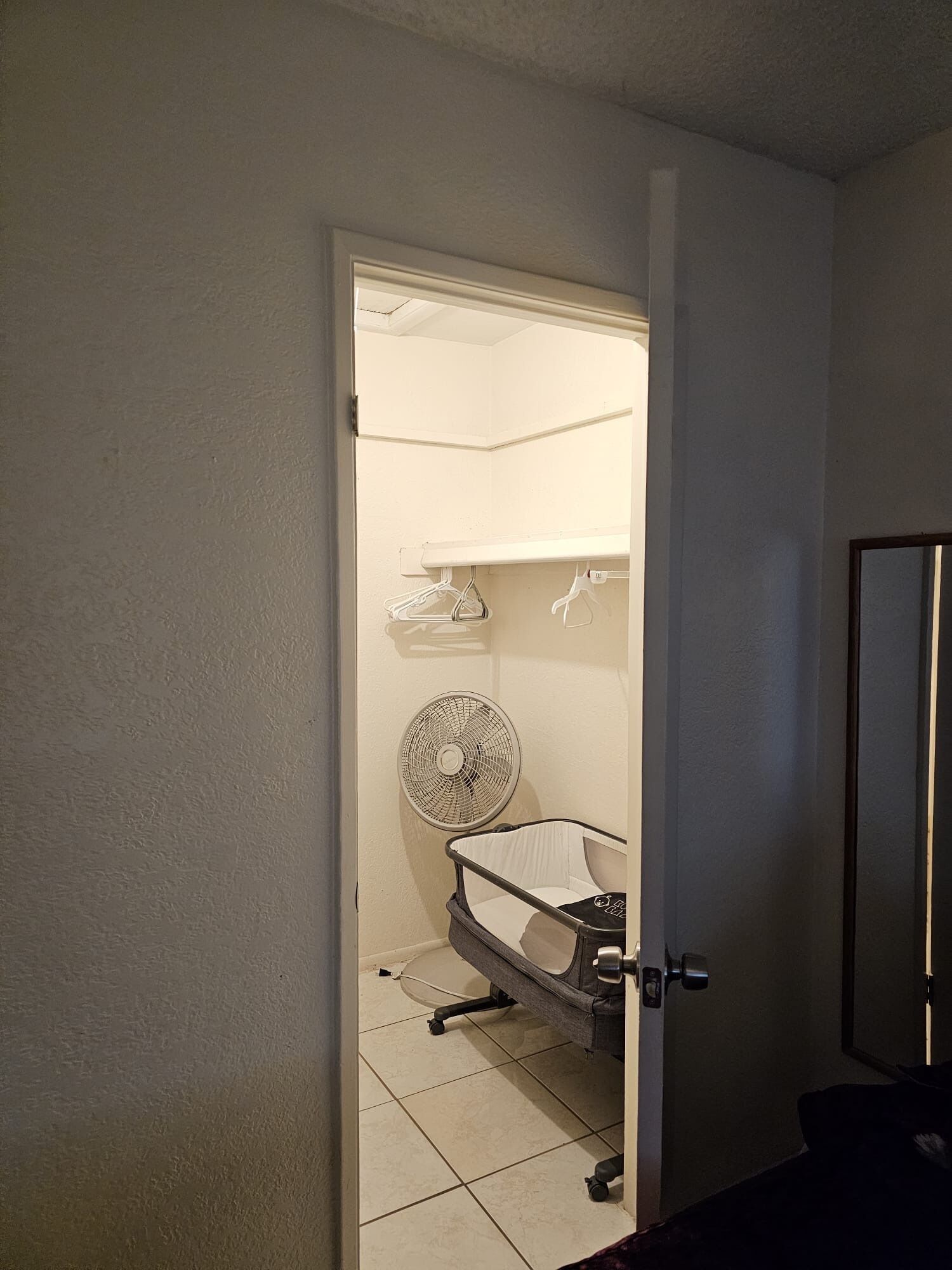 Ein Zimmer mit einer Tür zu einem Badezimmer, das einen weißen Ventilator, ein weißes Regal und einen weißen Stuhl enthält.