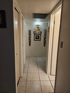 A hallway with tiled flooring, a vent on the ceiling, and two wall-mounted decorative panels.