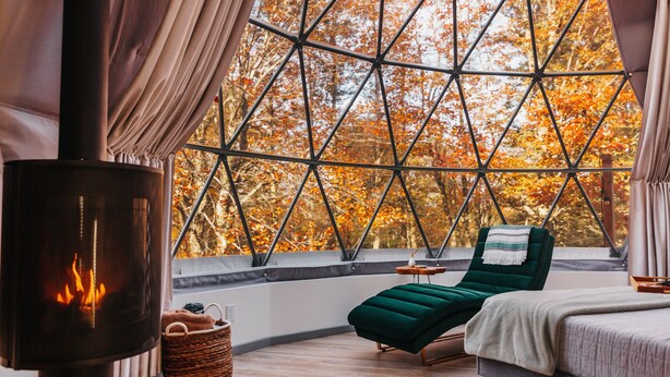 Une pièce confortable avec une grande fenêtre, une cheminée, un lit et un fauteuil.