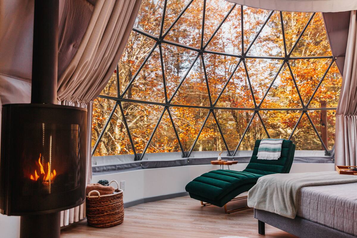 A cozy room with a large window, a fireplace, a bed, and a lounge chair.