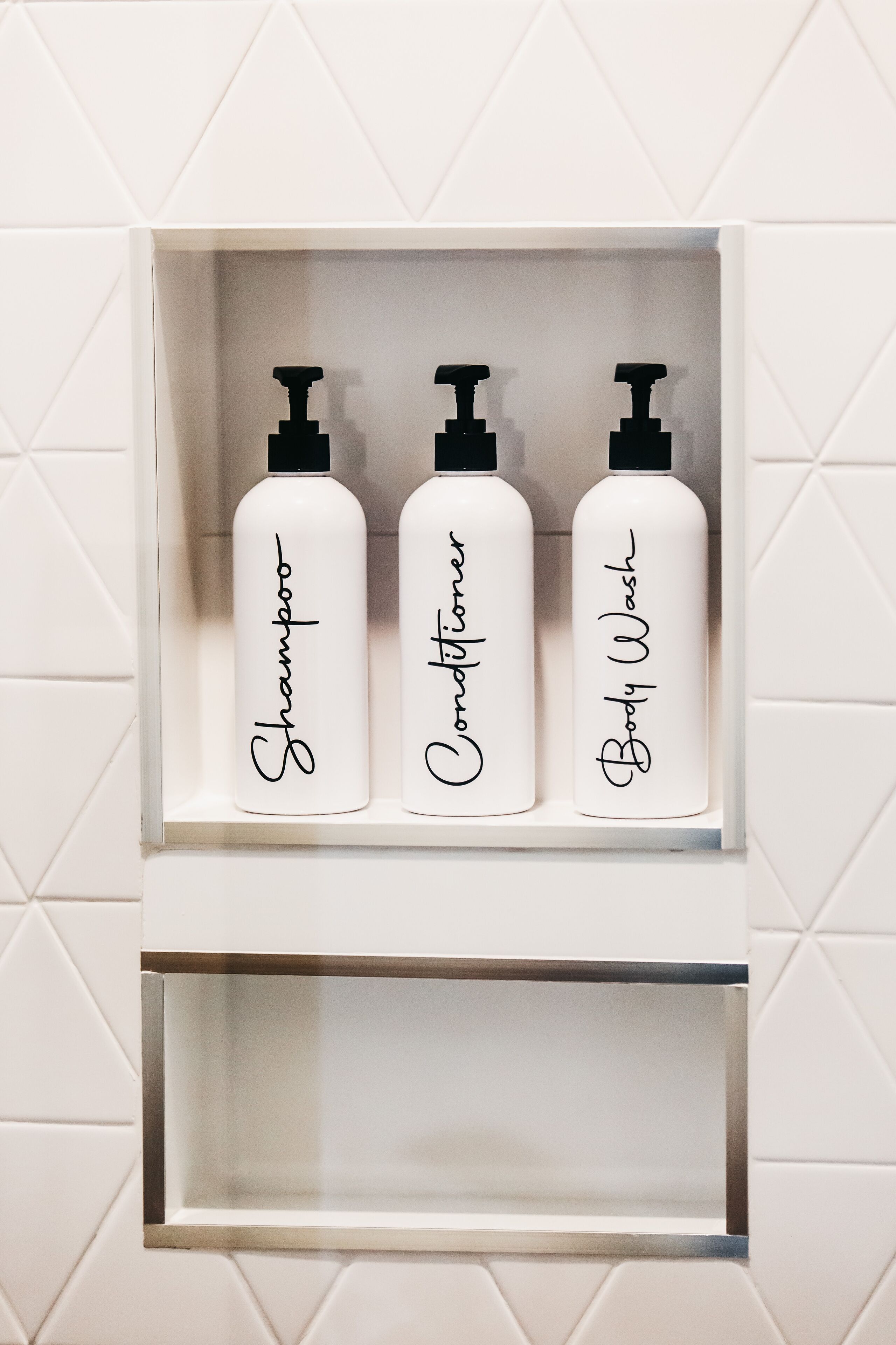 Een witte plank met drie flessen, gelabeld als ‘Shampoo’, ‘Conditioner’ en ‘Body Wash’.