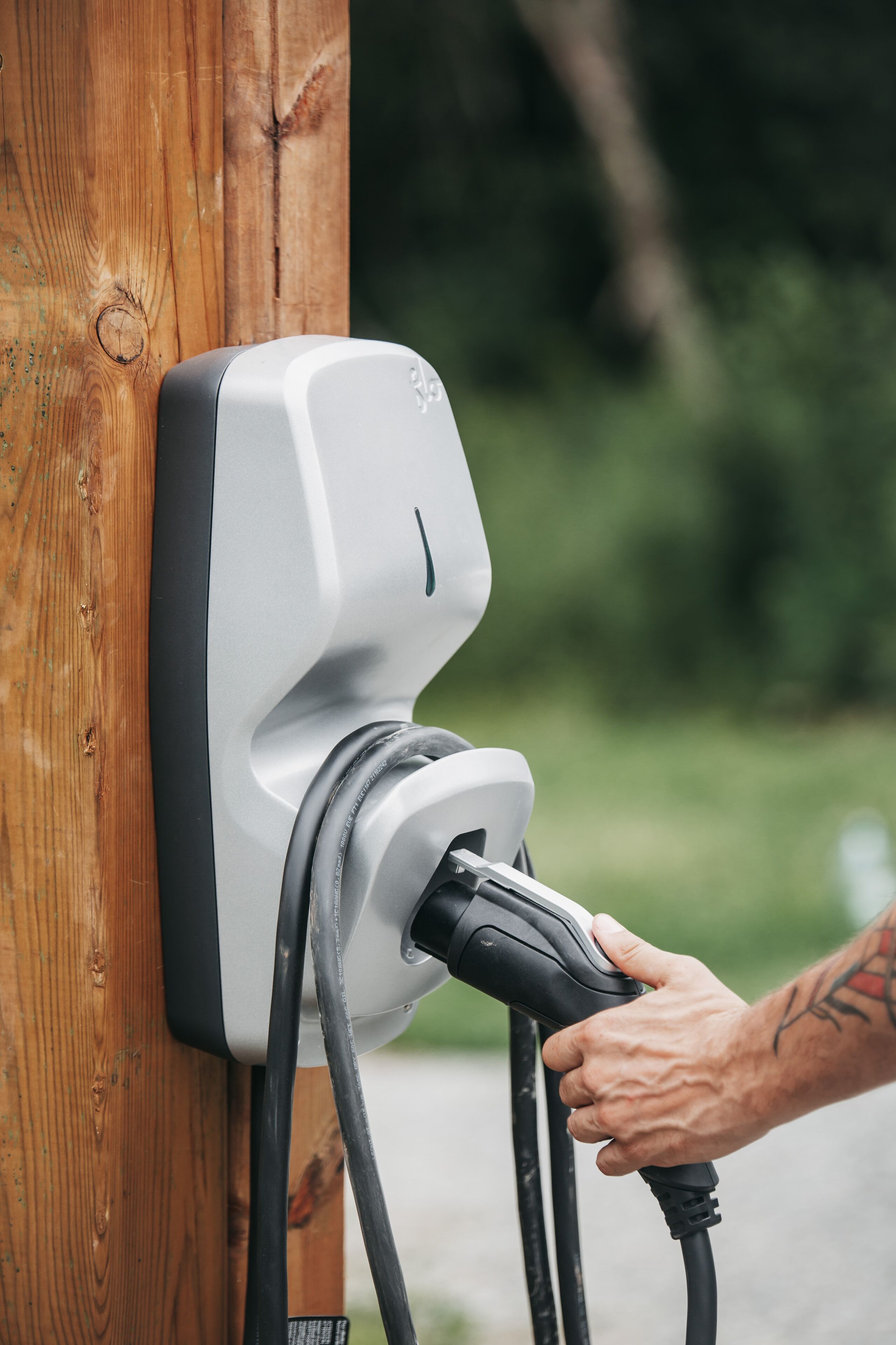 Una mano conectando un cargador de vehículo eléctrico a un poste de madera.