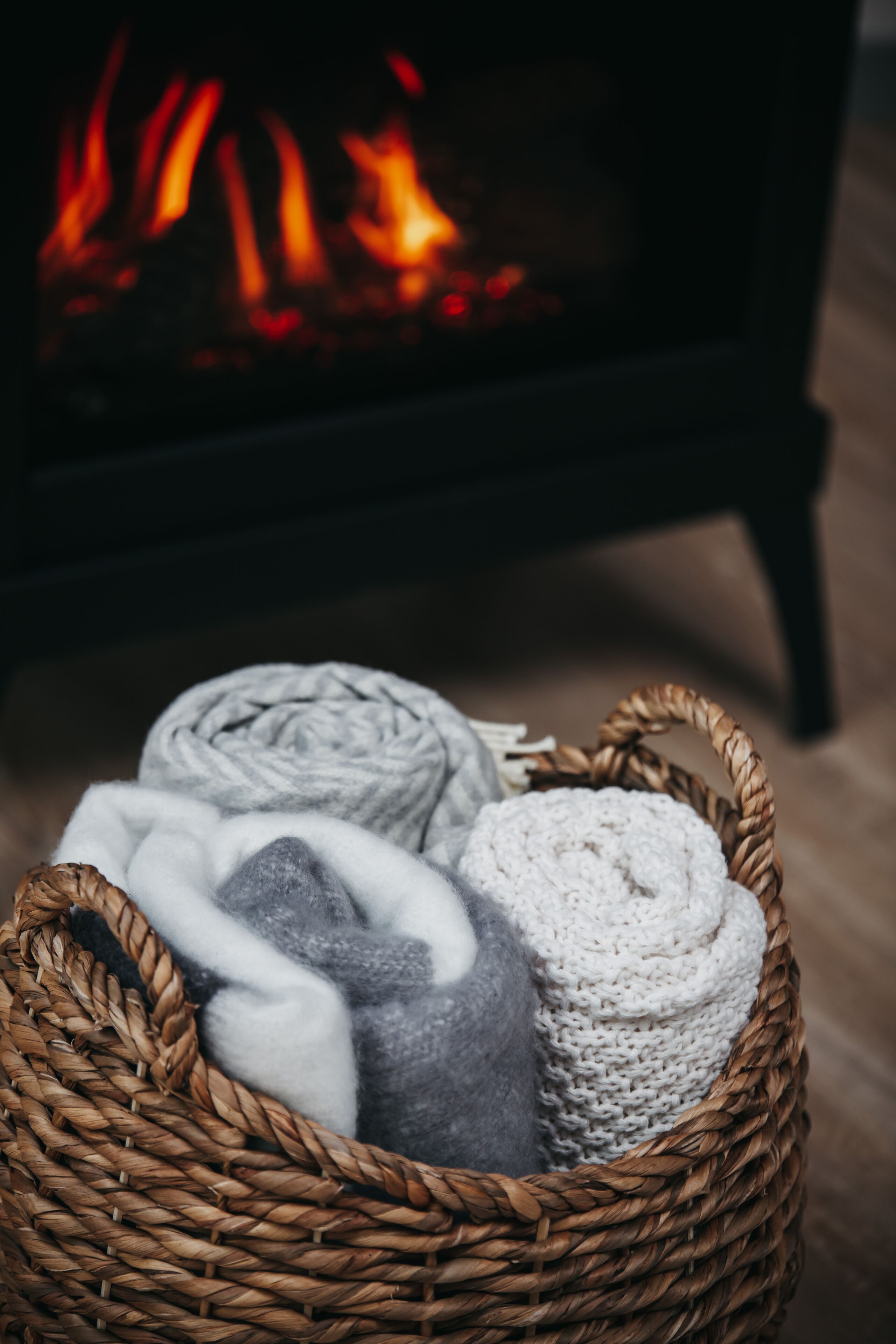 A wicker basket with rolled blankets and a fireplace in the background.
