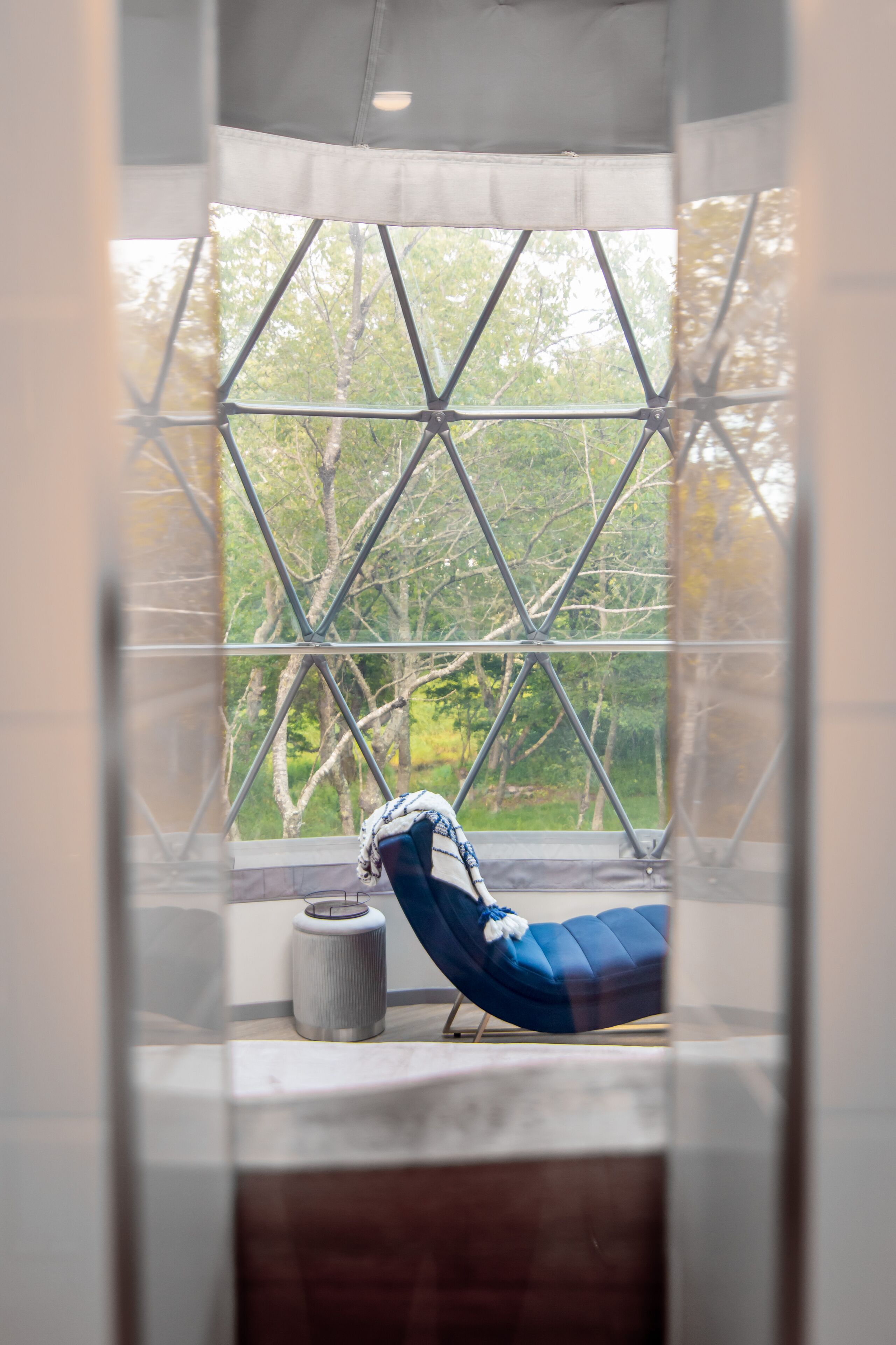 A room with a large window, a blue chair, and a cylindrical object on the windowsill.