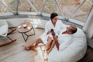 Um casal em um quarto aconchegante e moderno, com uma janela grande, uma mesa de madeira redonda e um espaço de estar confortável.