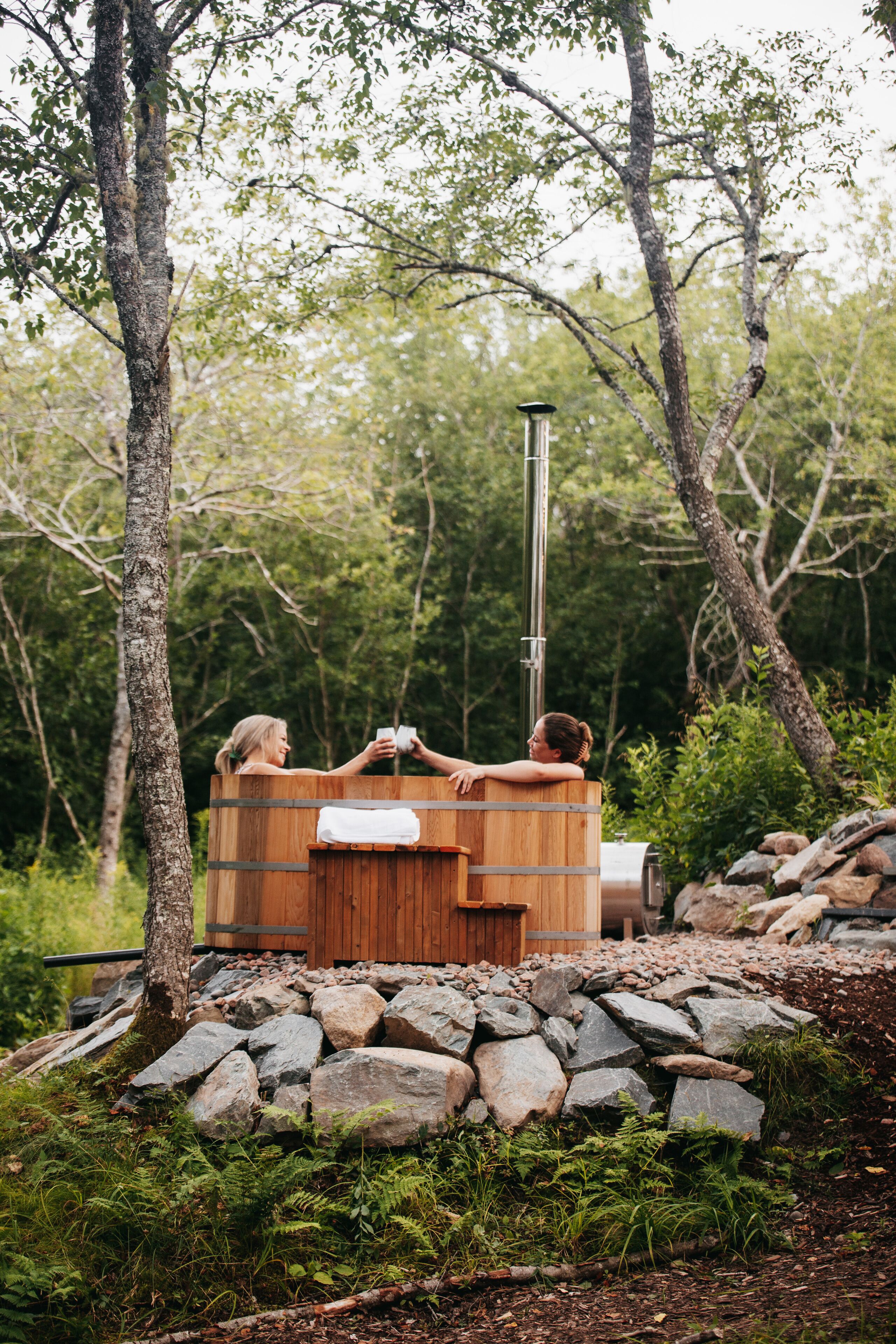 Un bain à remous en bois, entouré de rochers et de verdure, avec un poteau métallique à proximité.