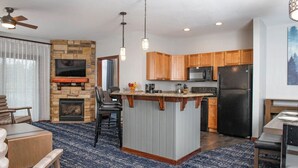 A modern kitchen with a stone fireplace, wooden cabinets, and a central island.