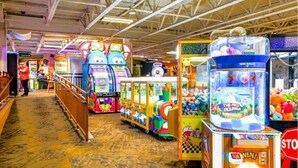 A row of colorful arcade games in a spacious indoor area with a high ceiling and a patterned floor.