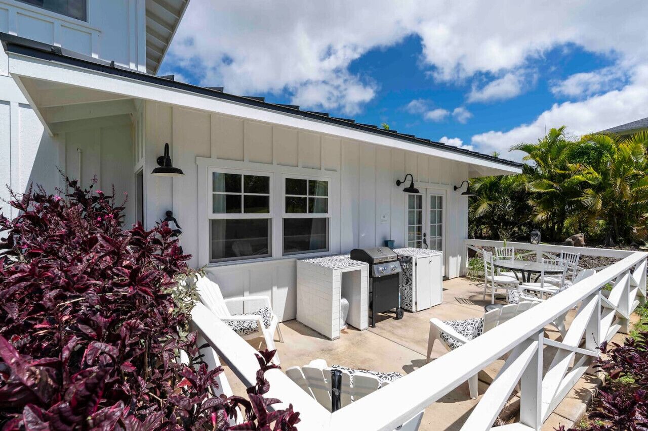 A white house with a patio area featuring a grill, outdoor seating, and a white fence.