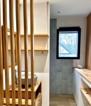 Eine moderne Küche mit Spüle aus Stein, Holzregalen und einem Fenster mit Blick auf kahle Bäume.