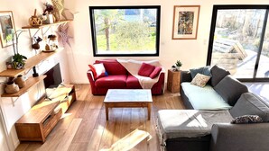 A modern living room with a red sofa, a grey sofa, wooden flooring, and large windows offering a view of the outdoors.