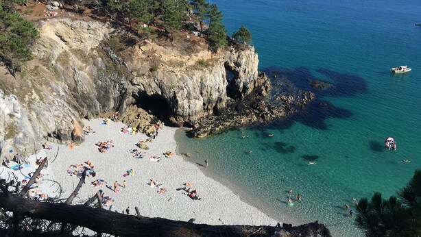 A coastal beach with rocky cliffs, clear turquoise waters, and a sandy shore.