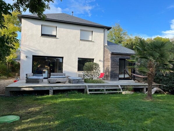 Ein modernes, zweigeschossiges Haus mit flachem Dach, großen Fenstern und einer überdachten Terrasse.