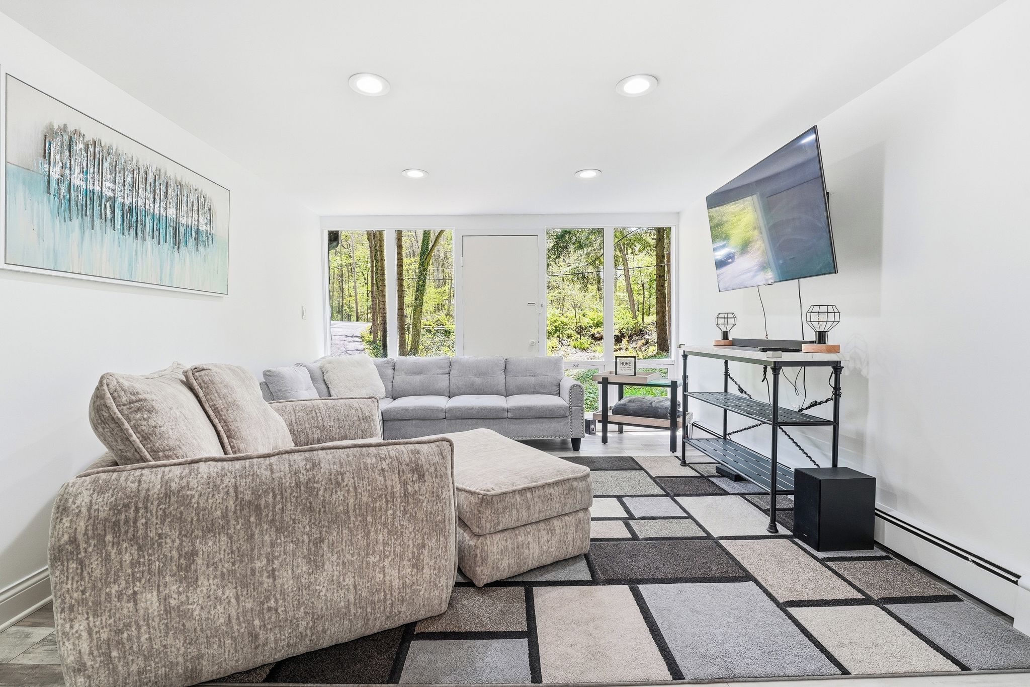 Un salon moderne avec un canapé gris, un pouf assorti et un téléviseur posé sur un meuble.